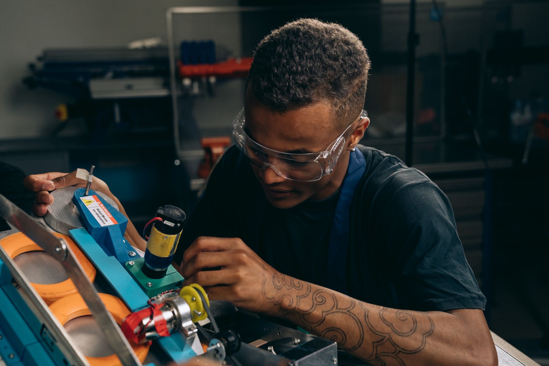 Focused young engineer wearing safety glasses adjusting machinery with precision in an industrial setting.