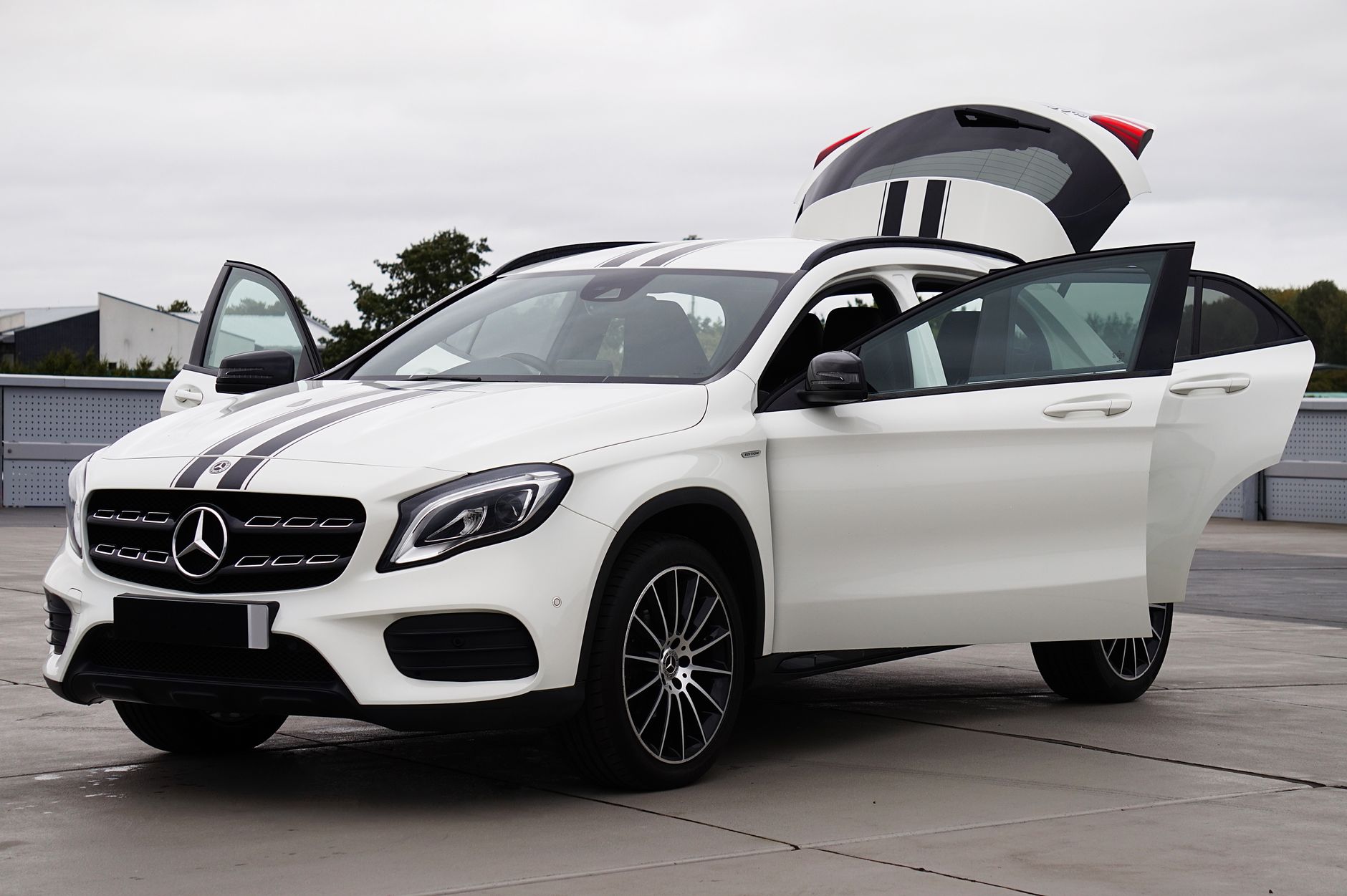 A sleek white Mercedes Benz GLA with open doors, showcased in an urban parking lot.