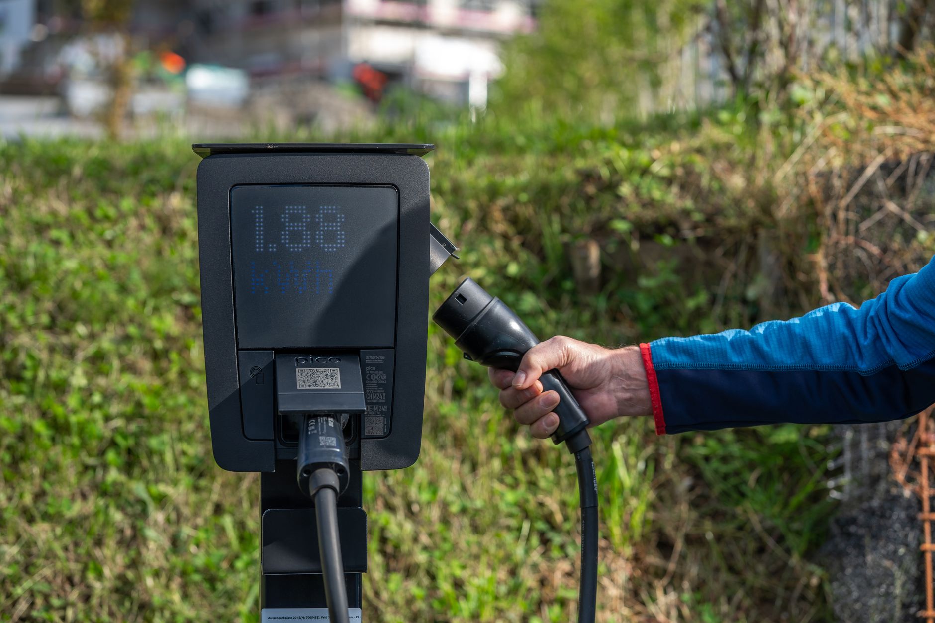 An outdoor electric car charging station with a hand holding a charging cable.