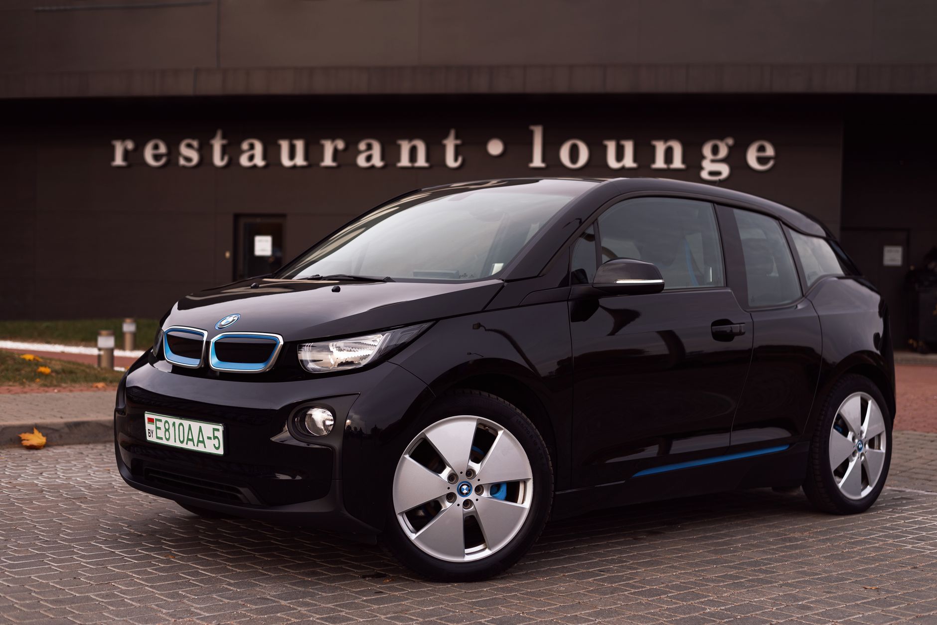Modern black electric vehicle parked outside a stylish restaurant-lounge in the city.