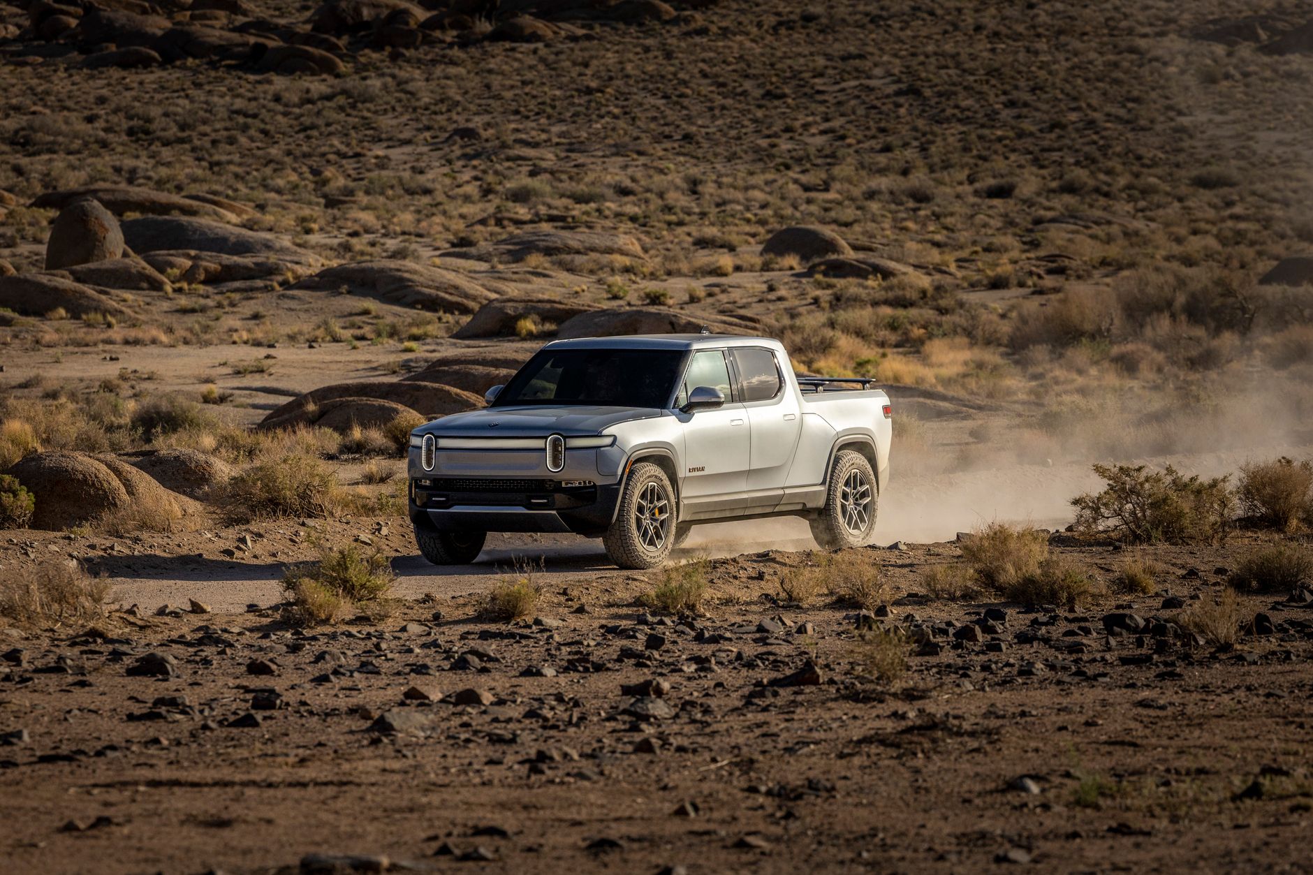 Electric pickup truck navigating a rocky desert landscape, showcasing off-road capability and rugged terrain.