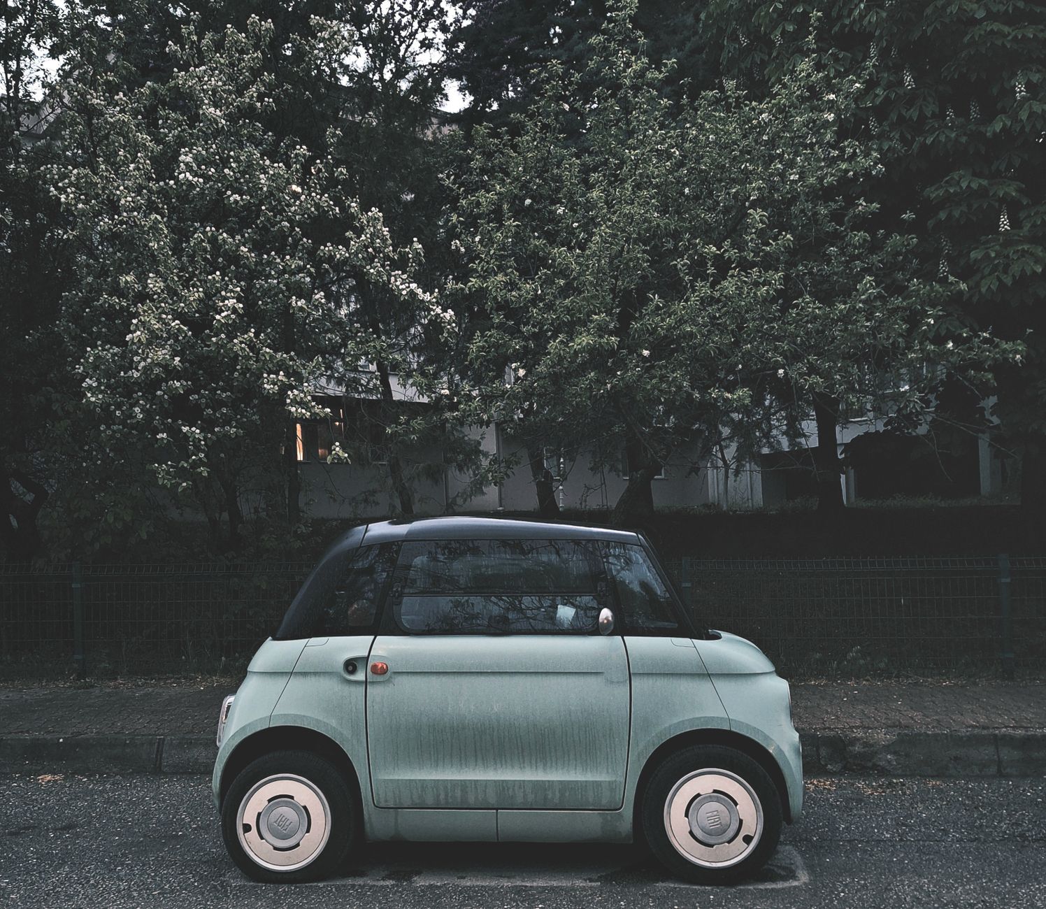 A modern compact electric car parked under blooming trees on a city street, highlighting urban eco-friendly transportation.