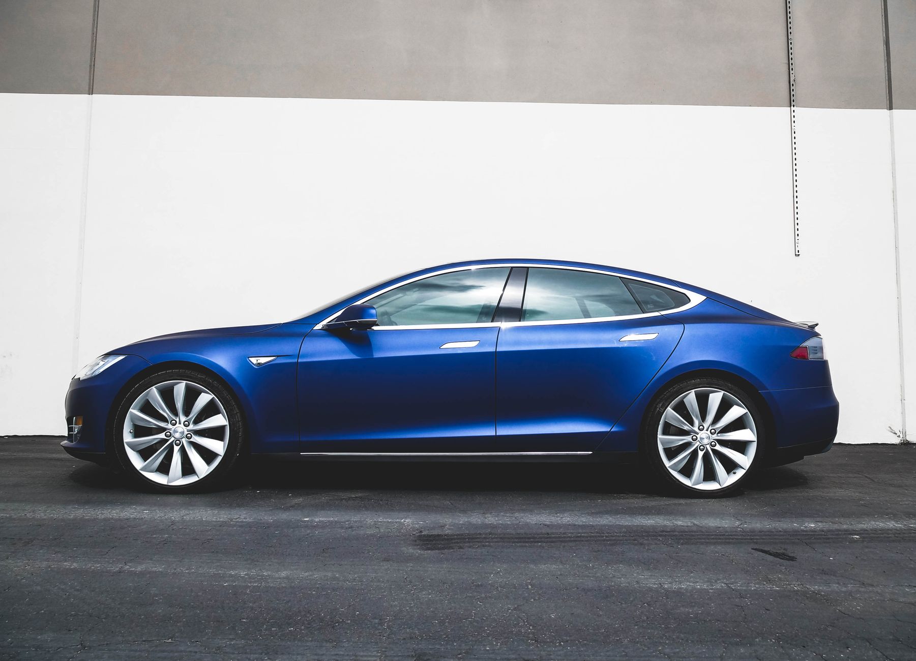 A modern blue electric car parked against a minimalist concrete wall, side view.