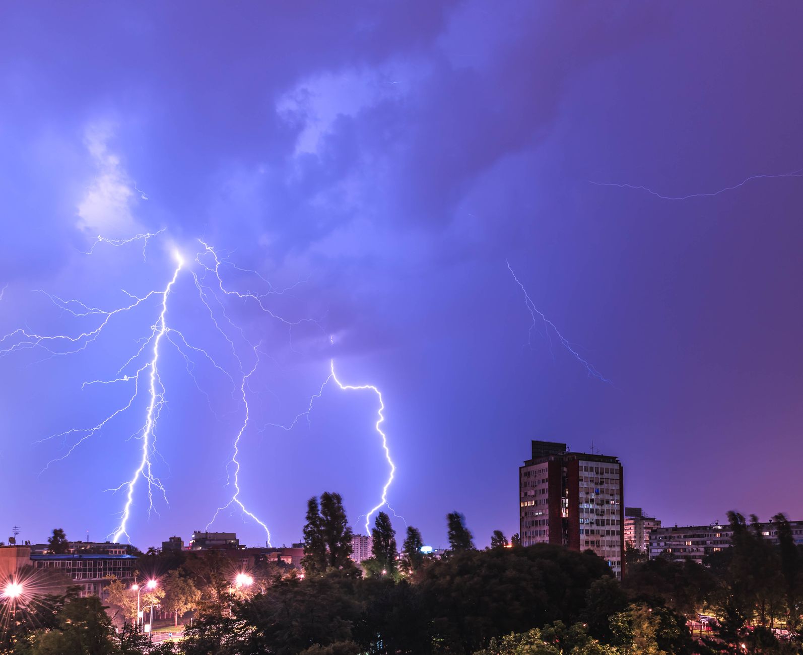 Vivid lightning bolt striking during a nighttime thunderstorm over a city skyline, capturing the power of nature.
