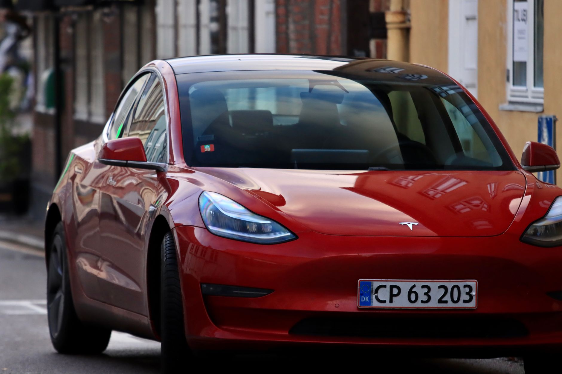 Striking red electric car with headlights on, parked on an urban street.