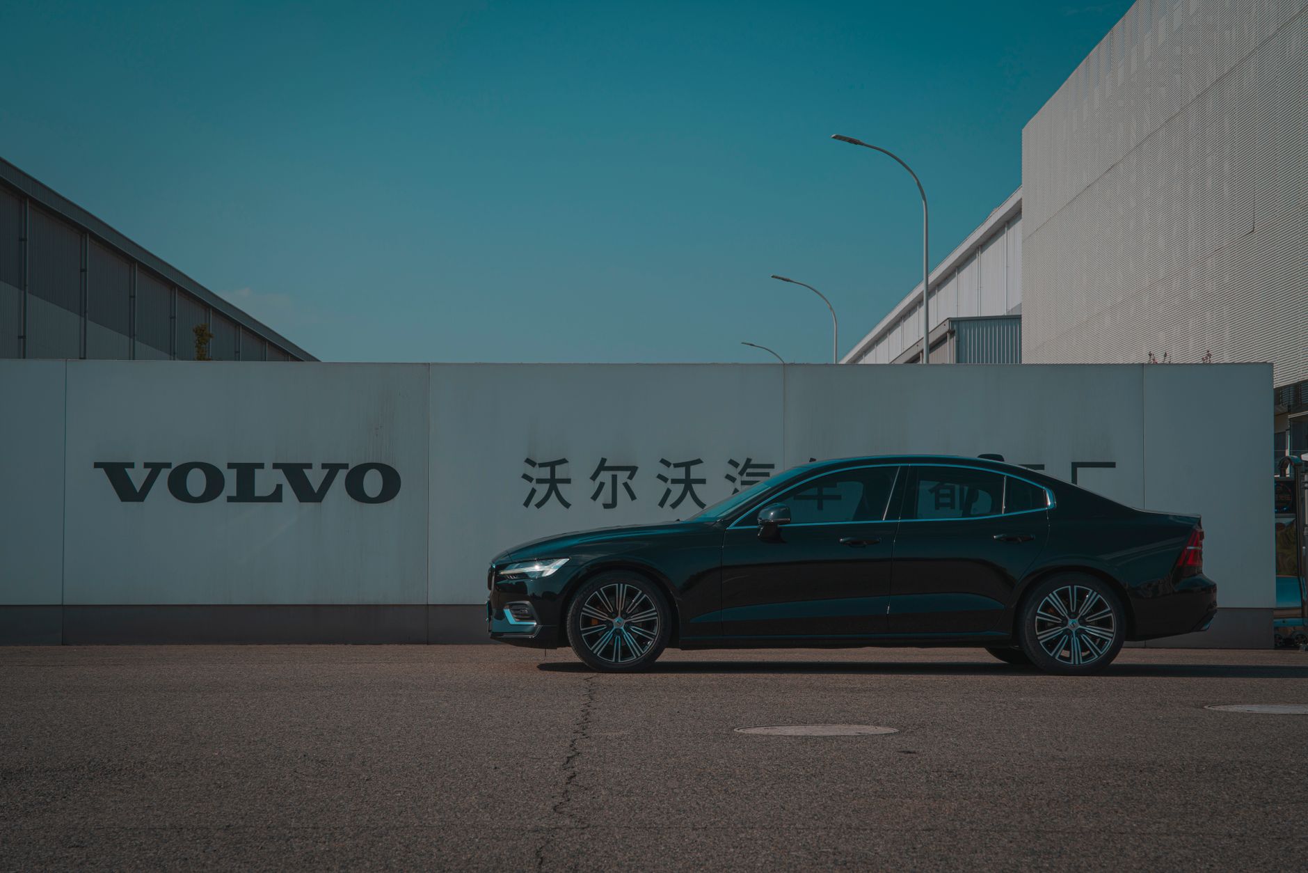 Sleek black Volvo sedan parked outside a manufacturing plant with Volvo signage.