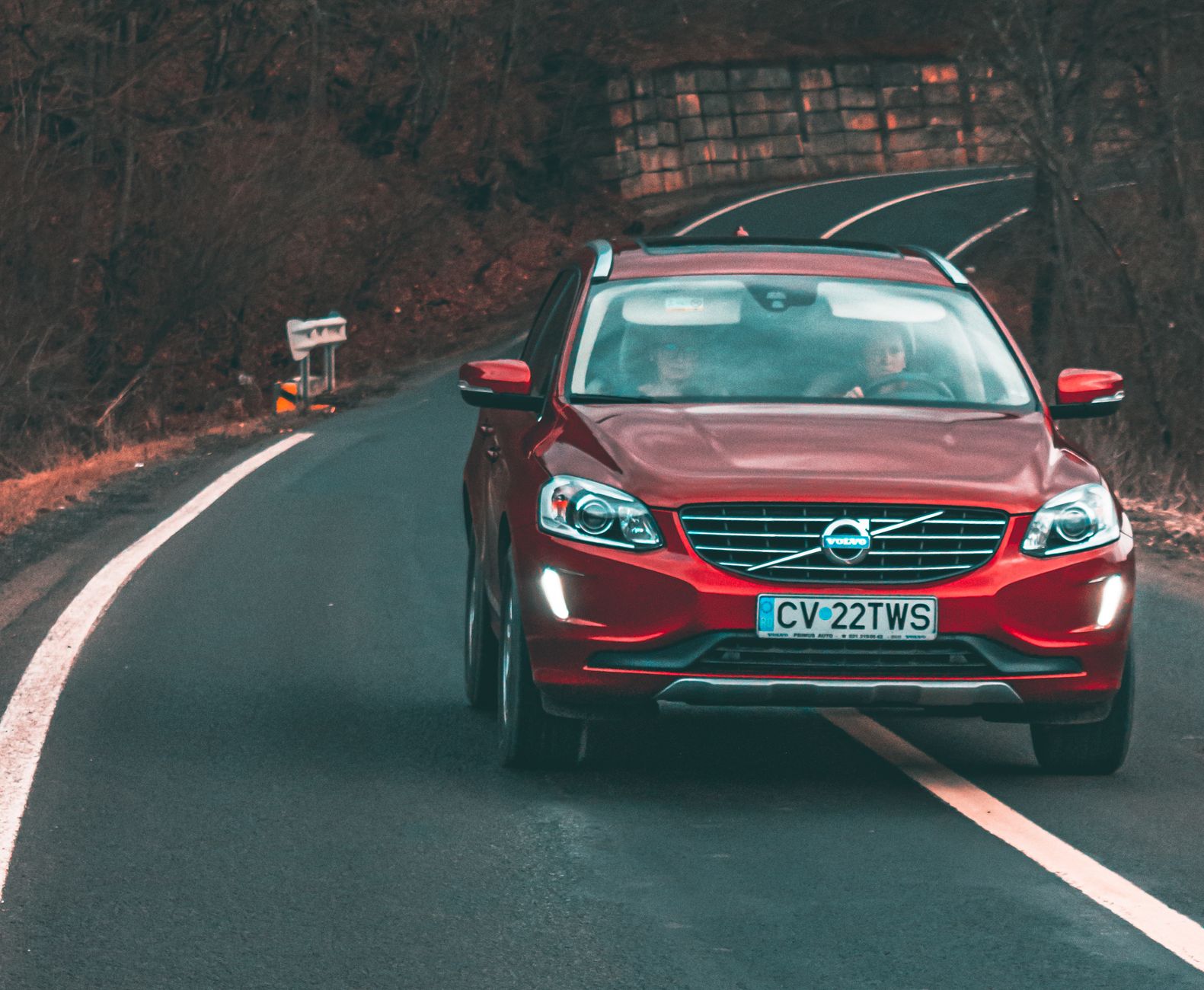 A red Volvo car drives along a curved road in Cătrușa, Romania, showcasing dynamic motion and scenic surroundings.