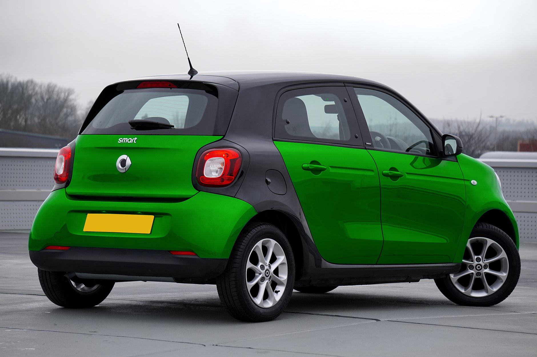 Bright green Smart car parked outdoors on a cloudy day.