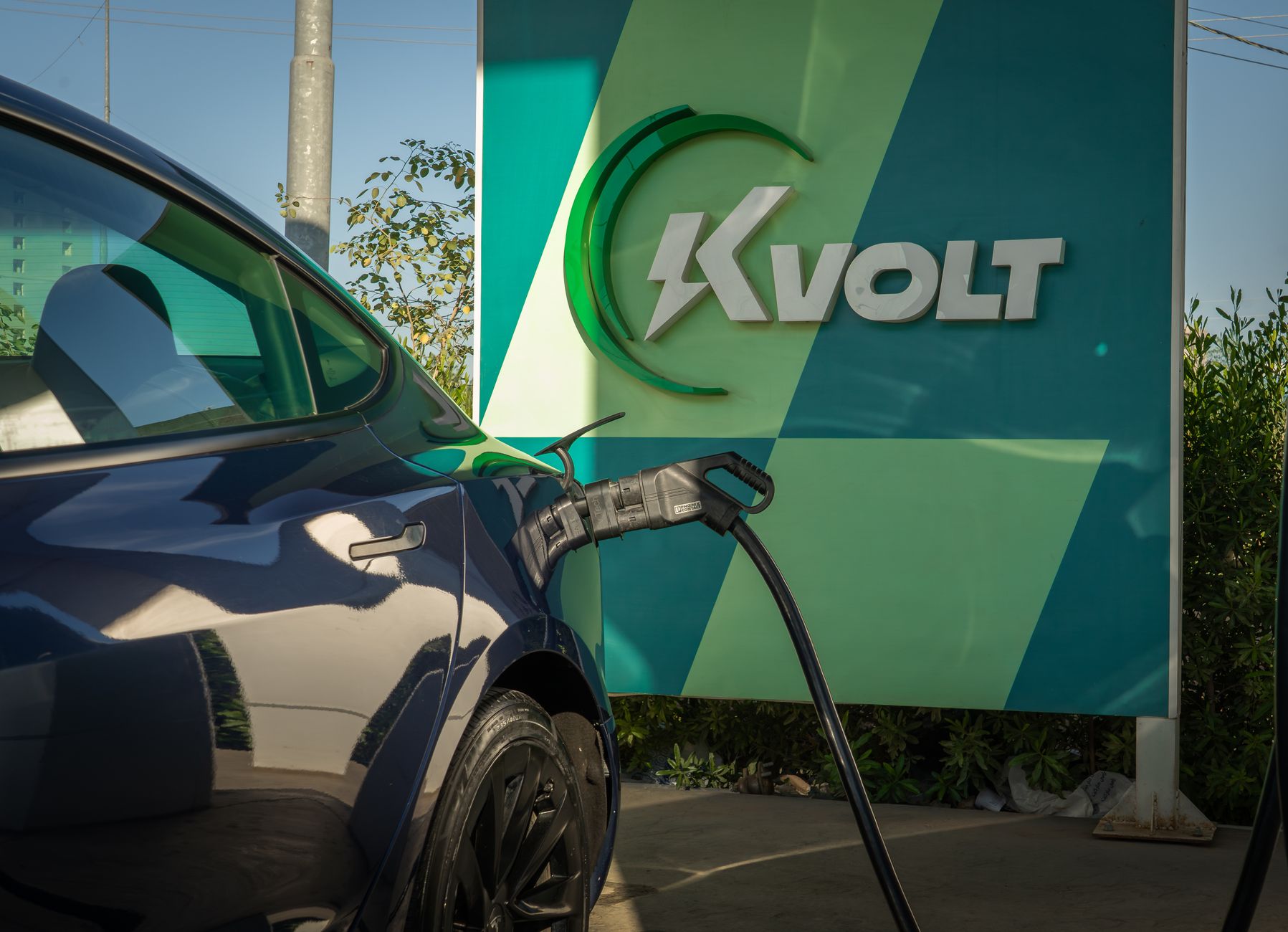 Electric car charging at Kvolt station under daylight, focus on modern eco-friendly vehicle.