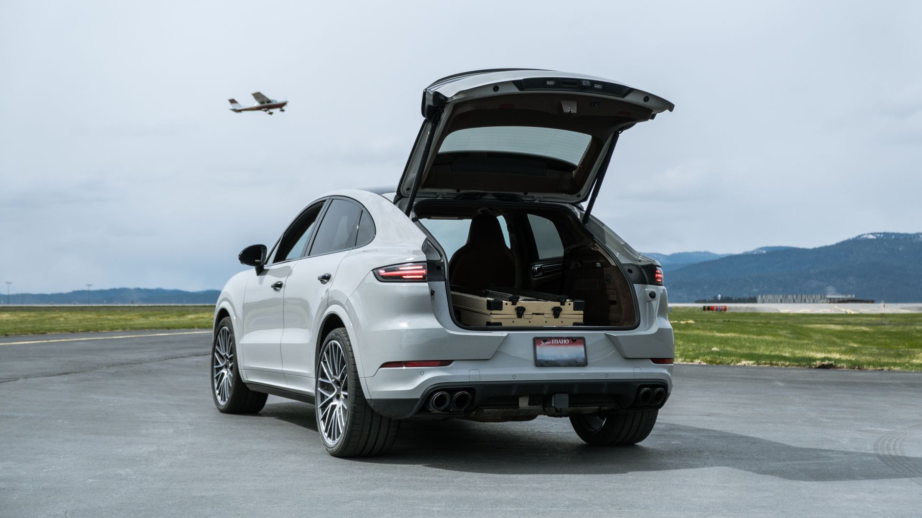White luxury SUV with an open trunk on an airport runway, plane taking off.