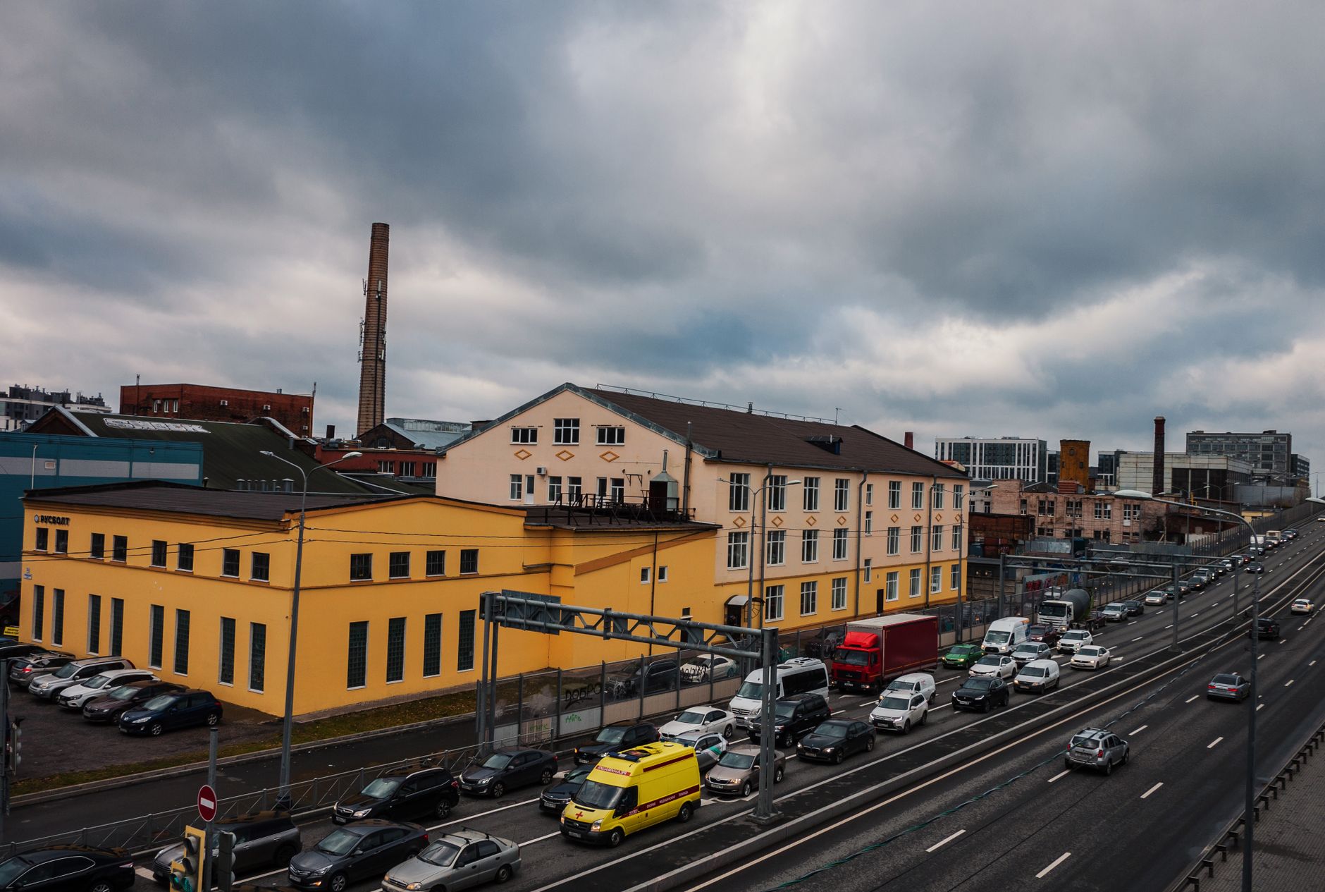 High-angle view of cars on a busy city road with industrial buildings under cloudy skies.