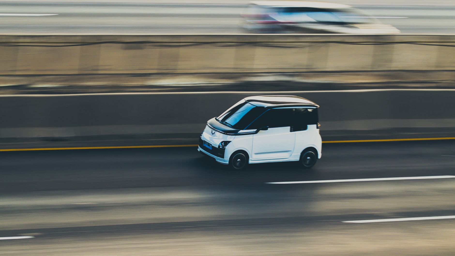 A white compact electric car is captured in motion on a highway using a dynamic panning technique.