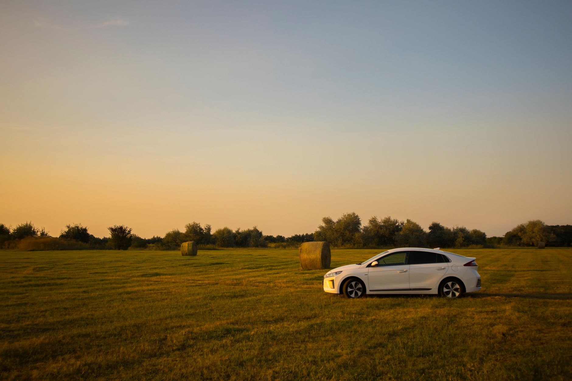 A white electric vehicle parked in a serene countryside field at sunset, showcasing eco-friendly travel.
