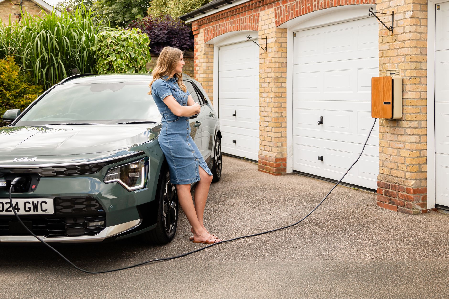 Woman charging electric vehicle at home with a modern wall-mounted charging station.