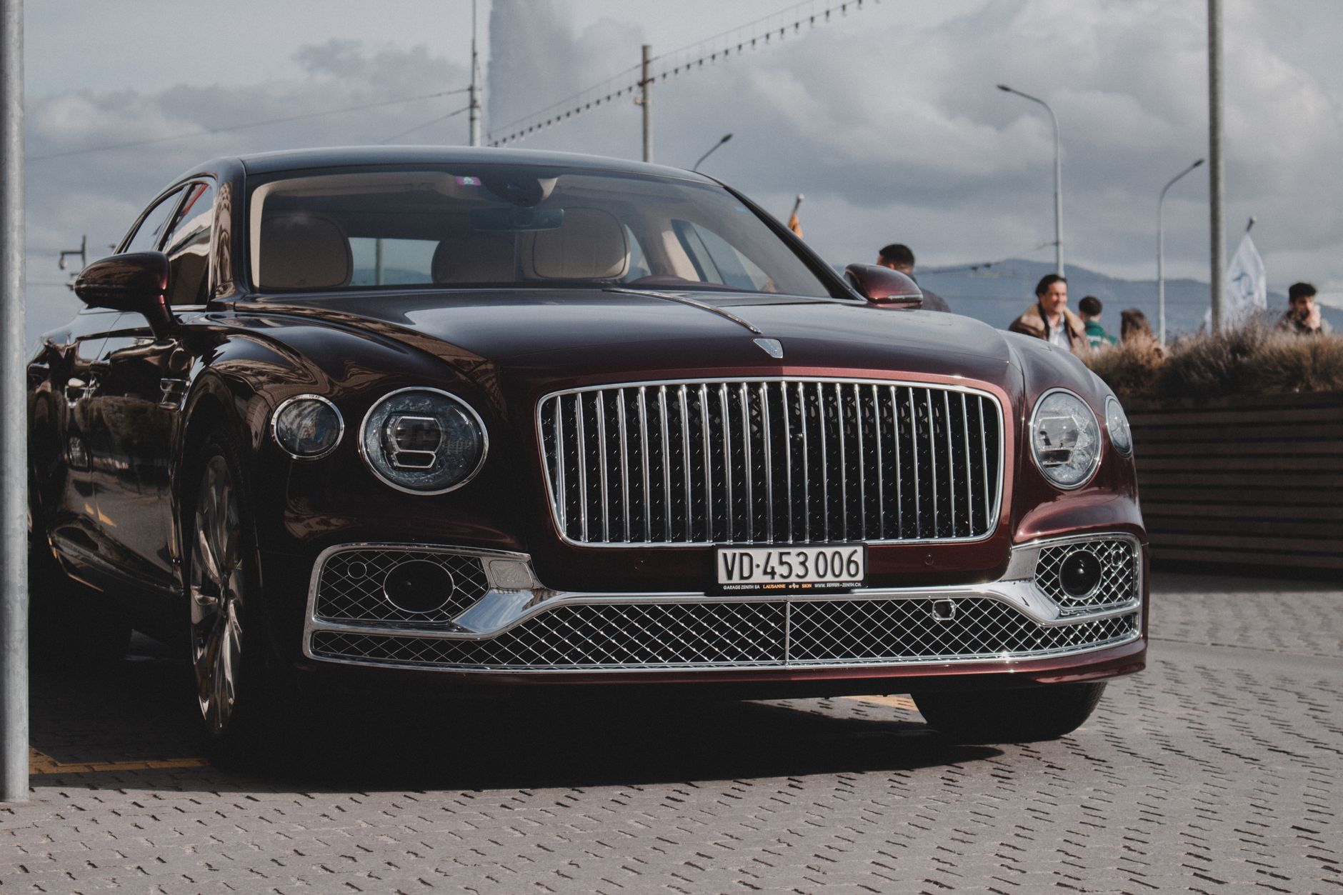 Front view of a shiny luxury Bentley car parked outdoors with people in the background.