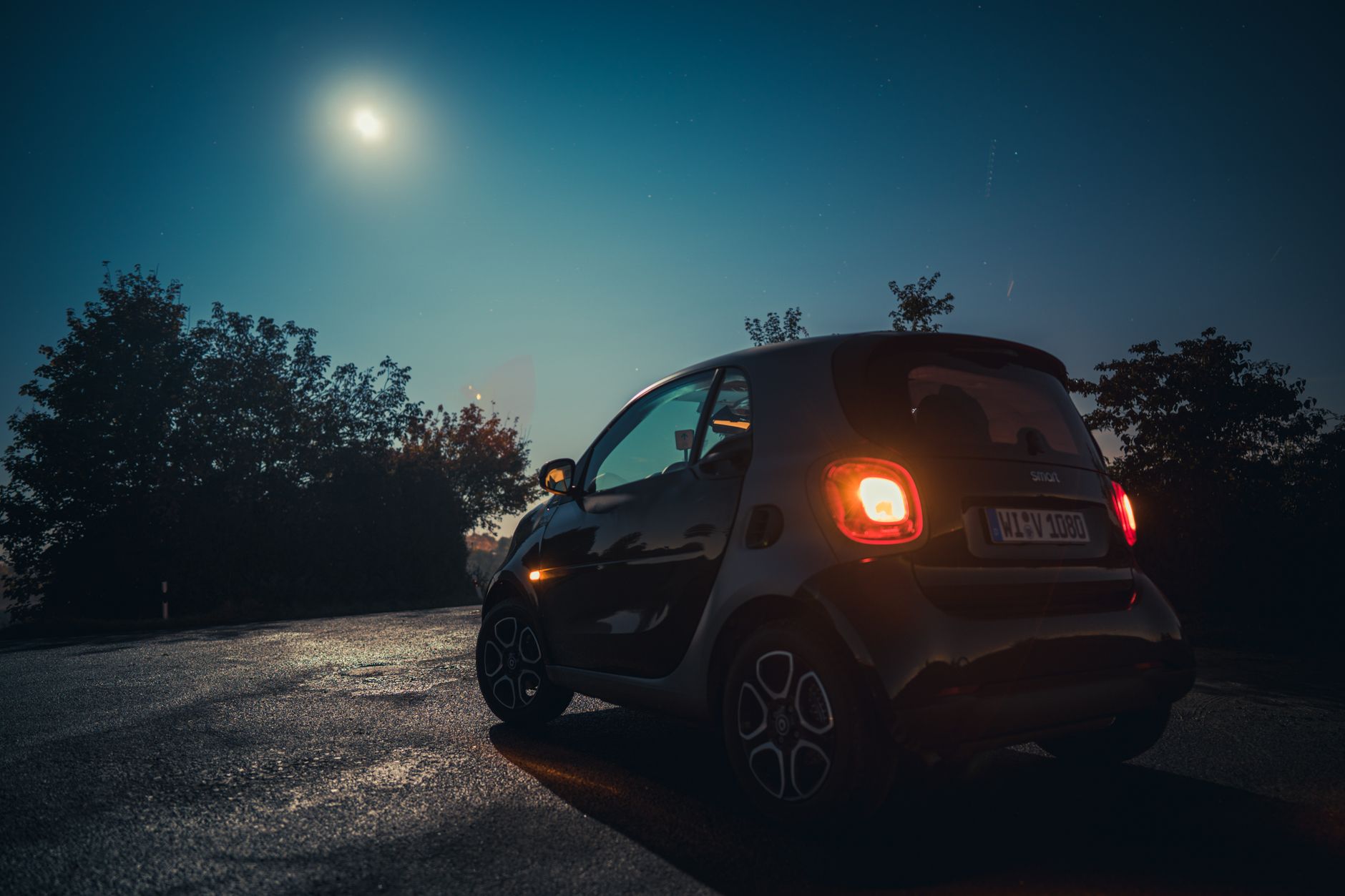 A sleek electric Smart Forfour parked outdoors at night, illuminated by a bright moon and street lights.