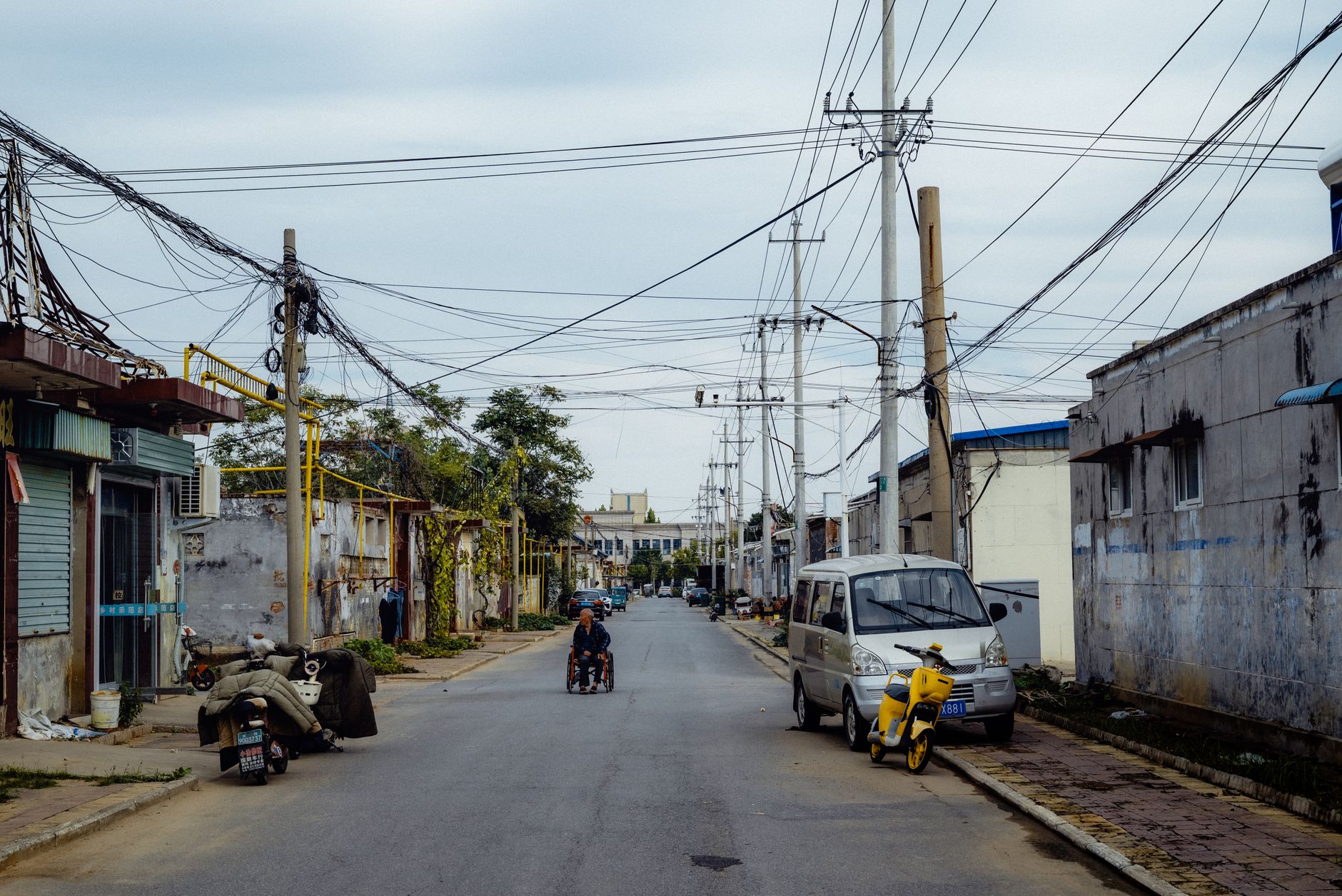 Quiet street with power lines, a van, and motorbikes in a rural town.