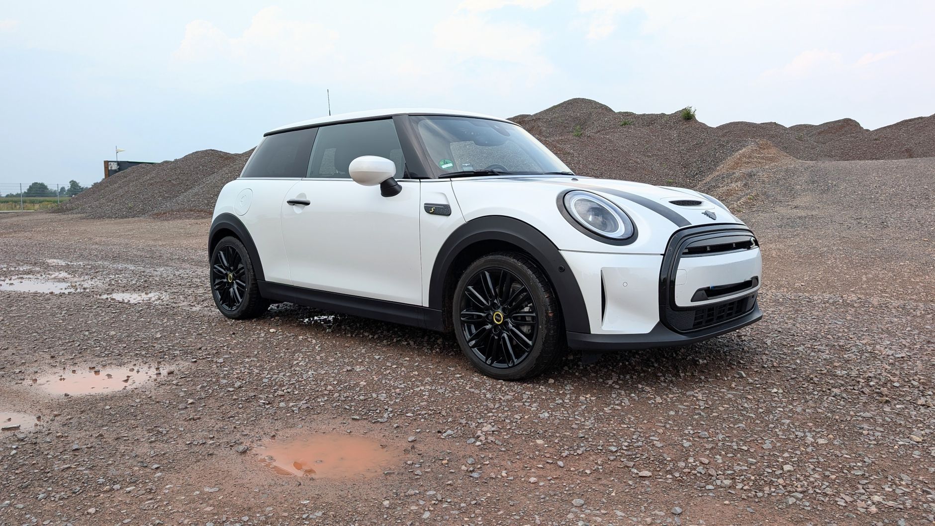 A white Mini Cooper S parked on a gravel lot with a clear sky.